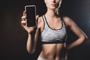 Siyah arkaplanda boş ekranlı cep telefonu gösteren kadın görüntüsü