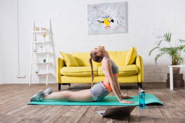 Spor kadının evdeki laptopun yanındaki spor minderinde gerinme görüntüsü