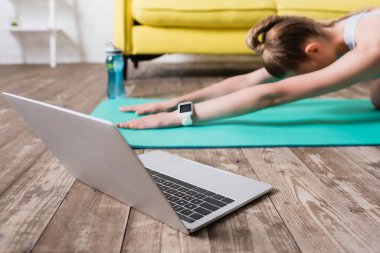 Spor kadının yakınındaki dizüstü bilgisayarın görüntüsü evde spor minderinin üzerinde geriniyor.