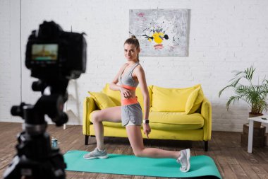 Evdeki dijital kameranın yanındaki fitness minderi üzerinde egzersiz yapan sporcu kadının seçici odağı 