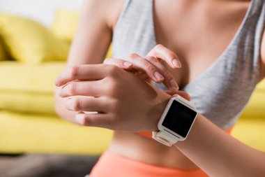 Cropped view of sportswoman touching smartwatch at home  clipart