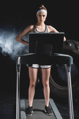 Spor merkezinde lastiğin yanındaki koşu bandında dumanla duran genç sporcu kadın. 