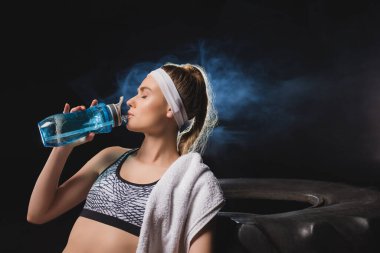 Spor salonunda havluyla su içen genç bir sporcu. 