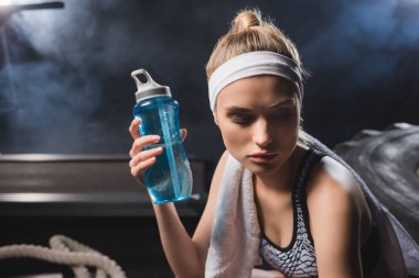 Spor salonunda havluyla spor şişesini dumanla tutan genç sporcunun seçici odağı. 