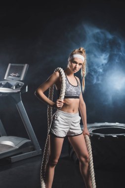 Spor salonunun seçici odak noktası savaş halatıyla lastik yakınındaki kameraya ve spor salonunda dumanla koşu bandına bakıyor. 