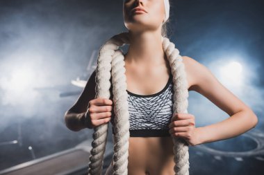 Saç bandı takmış sporcu kadının spor salonunda dumanlı halat tutuşu. 