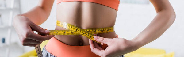 Панорамный снимок спортсменки, измеряющей тонкую талию лентой дома