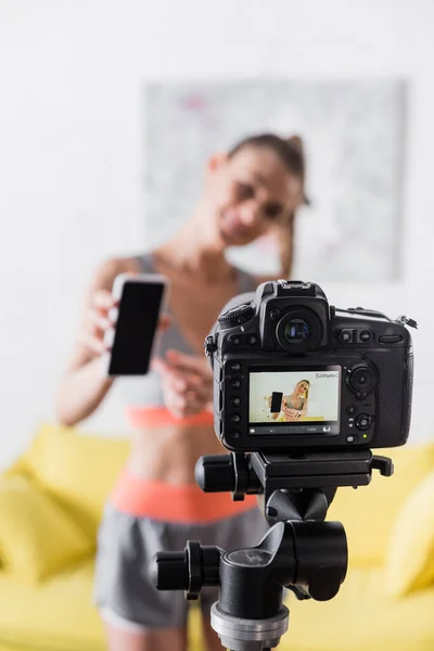 穿着运动服 手持智能手机 在家用数码相机旁使用空白屏幕的女性的选择性聚焦 — 图库照片
