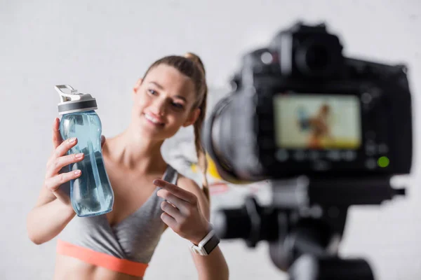 自宅でデジタルカメラの近くのスポーツボトルを指して陽気なスポーツ女性の選択的な焦点 — ストック写真