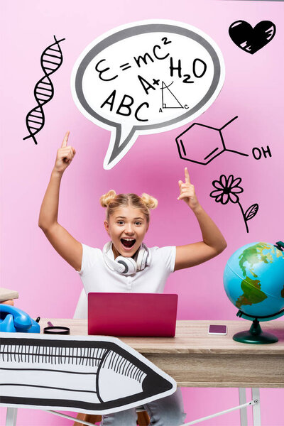 Excited kid pointing with fingers at speech bubble with illustration near laptop, smartphone and globe on pink
