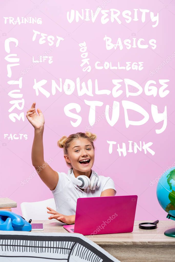 Schoolgirl sitting with raised hand near laptop, telephone, lettering and paper art on pink 