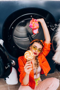 Çamaşırhanede lolipop ve giysi tutan şık bir kadının yüksek açılı görüntüsü