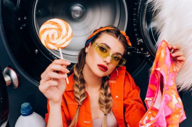 Çamaşırhanede lolipop ve giysi tutan genç, modaya uygun bir kadın.