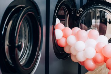 Çamaşırhanedeki modern çamaşır makinelerinin yanında ön planda bulanıklık olan pembe balonlar.