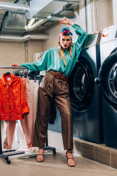 Trendige Junge Frau Turban Steht Neben Kleiderständern Und Waschmaschinen Modernen — Stockfoto