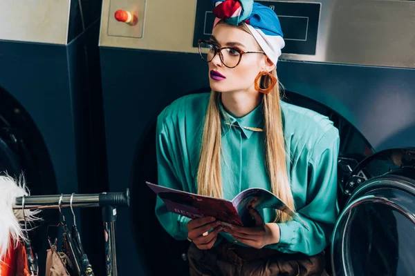 Jovem Mulher Turbante Óculos Segurando Revista Lavanderia — Fotografia de Stock