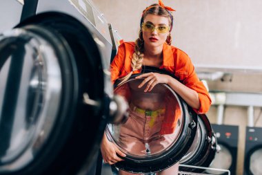 Saç bandı takmış şık bir kadın ve çamaşır makinesinin yanında güneş gözlüğü.