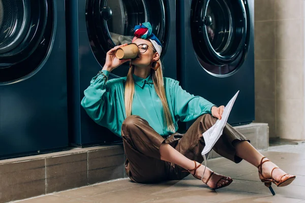 Trendy Woman Glasses Turban Holding Newspaper Drinking Coffee Laundromat — Stock Photo, Image