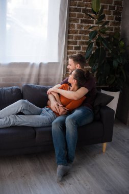young couple embracing while resting on sofa at home clipart