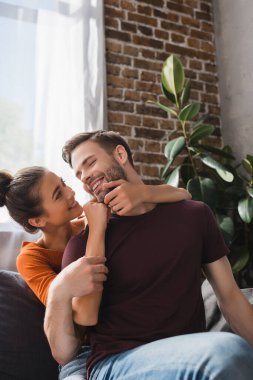 Mutlu kadın koltukta otururken neşeli erkek arkadaşının yüzüne dokunuyor.