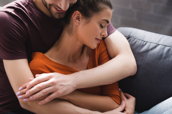 улыбающийся мужчина обнимает возлюбленную женщину сидя с закрытыми глазами вместе