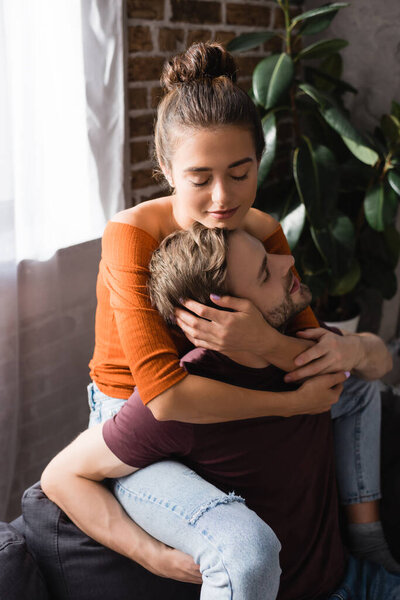 нежная женщина с закрытыми глазами обнимает молодого парня, сидя на диване