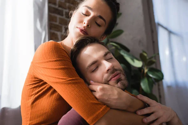 Jovem Casal Abraçando Com Olhos Fechados Enquanto Sentado Casa — Fotografia de Stock