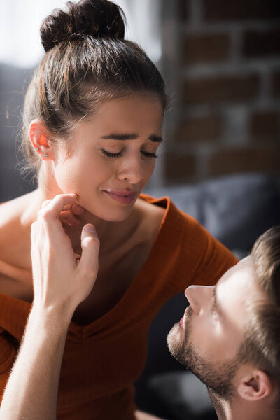 responsive man touching face of crying girlfriend while calming her at home