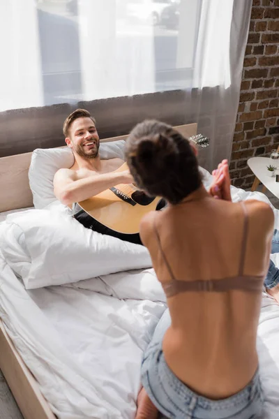 Smiling Man Lying Bed Playing Guitar While Looking Girlfriend Dancing — Stock Photo, Image