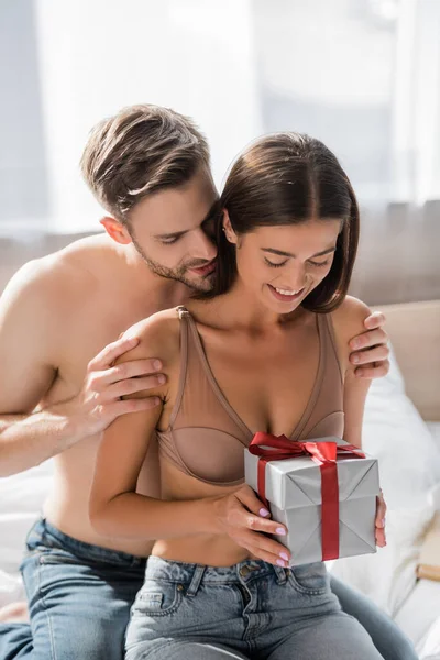 Shirtless Man Hugging Sexy Girlfriend Holding Gift Box Bedroom — Stock Photo, Image