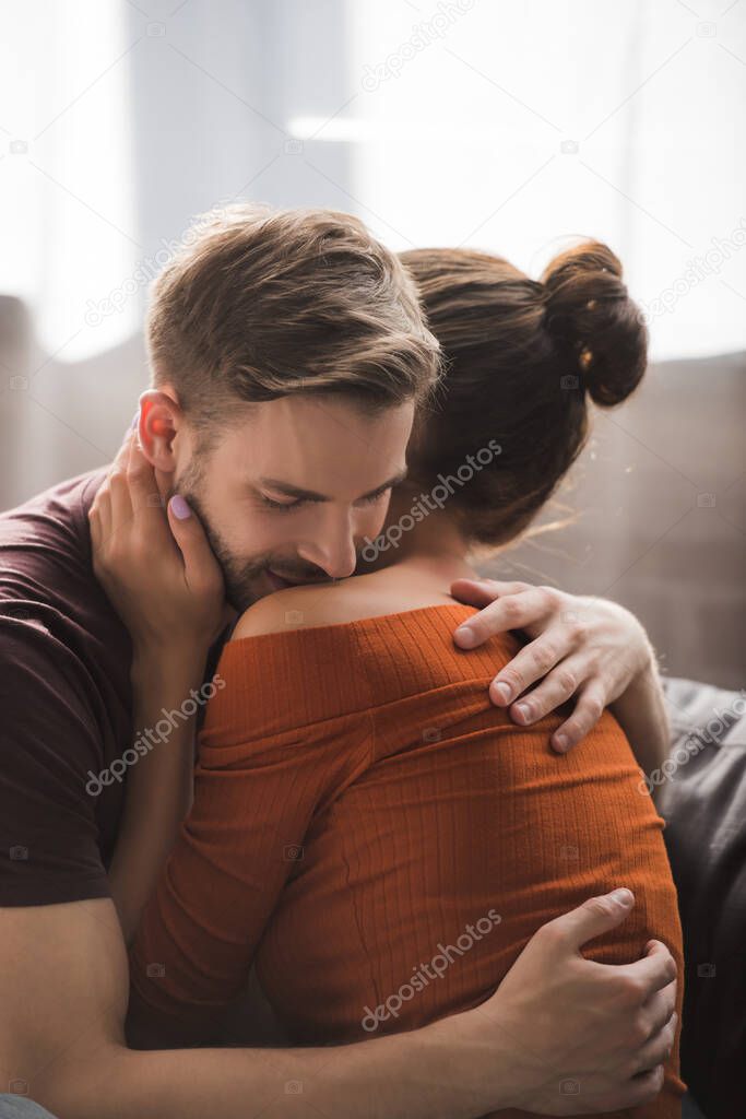 tender man hugging young girlfriend touching his neck while sitting at home