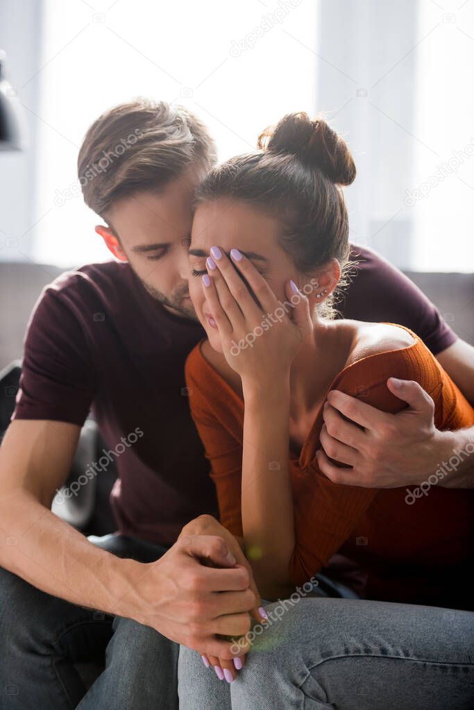 tender man calming depressed woman covering face with hand 