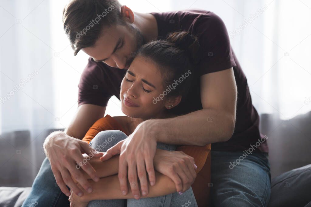 tender man calming frustrated girlfriend crying on sofa at home