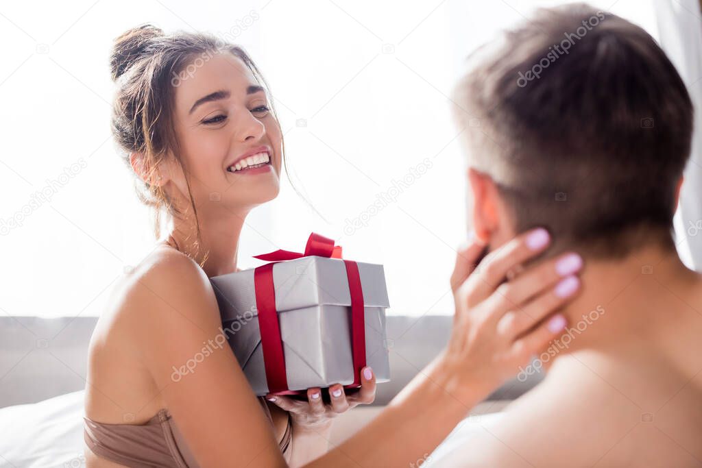 happy sensual woman holding gift box and touching man on blurred foreground