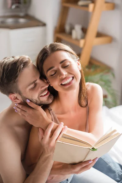 Happy Woman Closed Eyes Holding Book Touching Face Boyfriend Bedroom — Stock Photo, Image