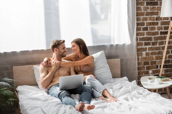 Mutlu Bir Kadın Yatakta Dizüstü Bilgisayar Kullanarak Üstsüz Erkek Arkadaşını — Stok fotoğraf