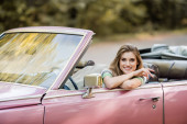 šťastná mladá žena sedí v retro kabriolet auto a usmívá se na kameru