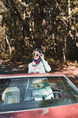 Stylish woman looking away from roofless car on blurred foreground on road  clipart