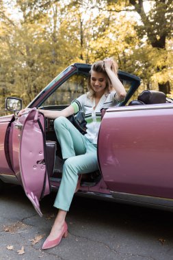 Cabriolet 'ten inerken saçlarına dokunan mutlu stil sahibi kadın.