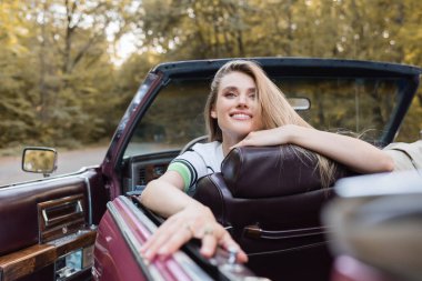 cheerful woman looking away while sitting in vintage cabriolet, banner clipart