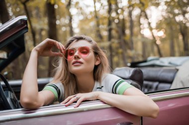 Cabriolet 'te otururken güneş gözlüklerine dokunan şık bir kadın.