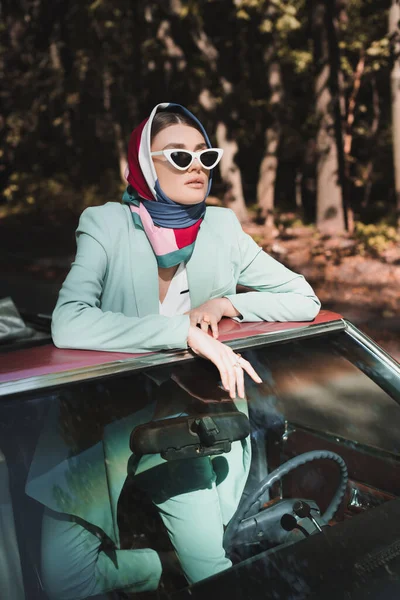 Stylowa Kobieta Okularach Przeciwsłonecznych Chustce Odwracając Wzrok Zabytkowego Samochodu Bez — Zdjęcie stockowe