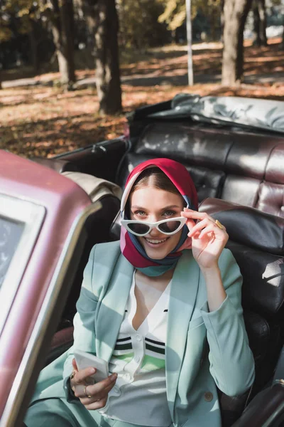 Woman Holding Sunglasses Smartphone Roofless Car Blurred Foreground Outdoors — Stock Photo, Image