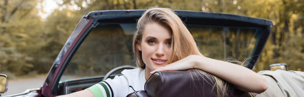 young smiling woman looking at camera while sitting in convertible car, banner