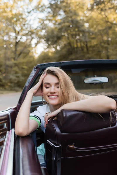 Happy Woman Touching Head While Sitting Cabriolet Closed Eyes Blurred — Stock Photo, Image