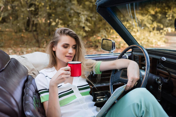 молодая женщина смотрит на дорожную карту, сидя в котелке с чашкой кофе