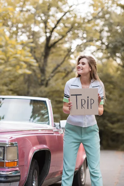 Cheerful Woman Looking Away While Holding Card Trip Lettering Vintage — Stock Photo, Image