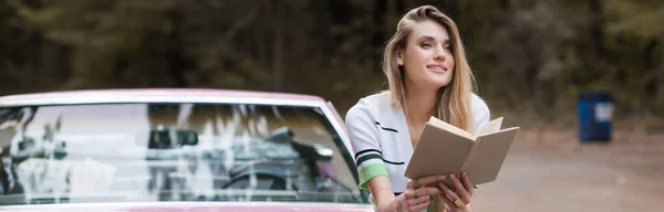 Donna Sorridente Seduta Auto Con Libro Guardando Lontano Sfondo Sfocato — Foto Stock