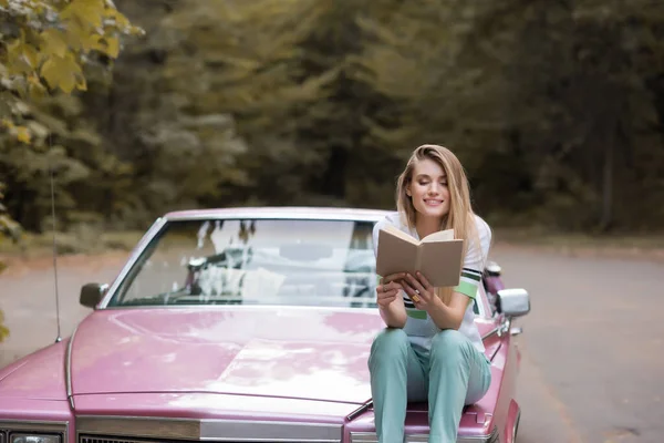 Glückliche Junge Frau Liest Buch Während Sie Auf Der Motorhaube — Stockfoto