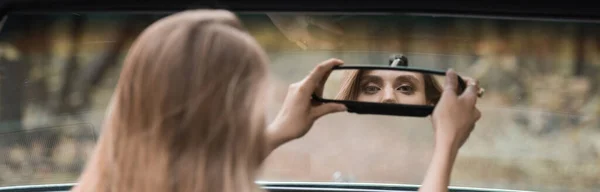 后视镜年轻女子调整后视镜在汽车上模糊的前景 — 图库照片